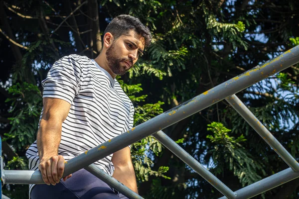 Parkta barda egzersiz yapan çekici bir genç adam kol egzersizi yapıyor.