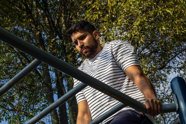 Parkta barda egzersiz yapan çekici bir genç adam kol egzersizi yapıyor.