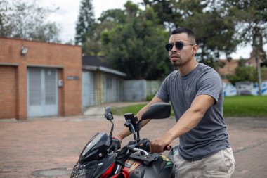 Motosikletli, gözlüklü, motosikletli genç bir adam yolda motosiklet gezisine başlamak üzere.