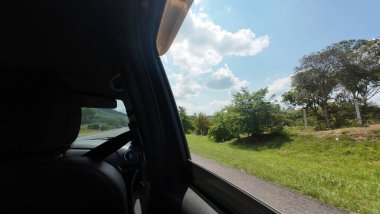 Güneşli bir günde, arka planda dağları ve ormanı olan bir yolda yürüyen bir arabayla seyahat eden aile.