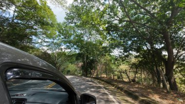 Güneşli bir günde, arka planda dağları ve ormanı olan bir yolda yürüyen bir arabayla seyahat eden aile.