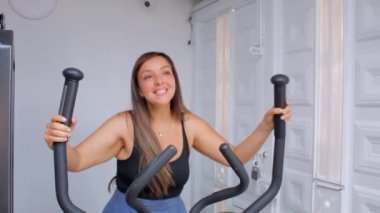 Spor salonunda eliptik bir makinede egzersiz yapan genç ve mutlu bir fitness kadını.