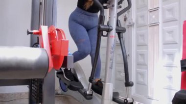 Spor salonunda eliptik bir makinede egzersiz yapan genç ve mutlu bir fitness kadını.