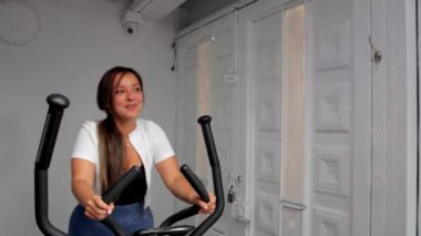 Spor salonunda eliptik bir makinede egzersiz yapan genç ve mutlu bir fitness kadını.