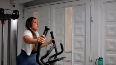 Spor salonunda eliptik bir makinede egzersiz yapan genç ve mutlu bir fitness kadını.