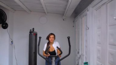 Spor salonunda eliptik bir makinede egzersiz yapan genç ve mutlu bir fitness kadını.