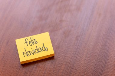 Ahşap masa arkasında yapışkan bir not. Yazılı not: Mutlu Noeller.