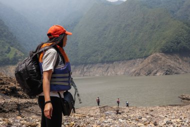 Bavulu ve şapkası olan genç bir kadın tatilde Rocky Dağı 'nda bir gölün kenarında yürüyor.