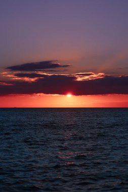 Manzara nefes kesici bir gün batımı, durgun okyanusa sıcak bir parıltı saçan turuncu ve sarı tonlarıyla gökyüzünü boyar..