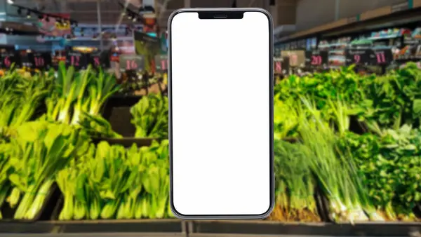 holding blank screen for text on smartphone, mobile, cell phone with blurry vegetable shelf background.,  supermarket Blank screen mobile phone for graphic display montage.