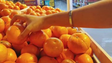 Kadınların eli pazarda meyveleri olan renkli portakalı bir raftan seçiyor ve yakından çekiyor. Süpermarket kavramı