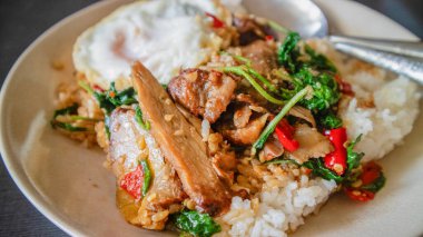 Kutsal fesleğenle karıştırılmış ördek güzel ördek eti, altın rengi kahverengi. Sarımsak ve fesleğen, ahşap bir masada beyaz bir tabağa yerleştirilmiş kırmızı biber, sarımsak ve fesleğen yaprakları, Tayland yemeği.