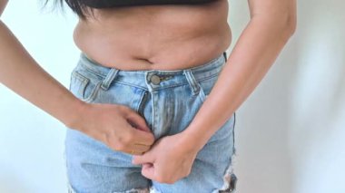 Kilolu bir kadın karnını sıkıyor ve aşırı kilolu olduğu için kendini kötü hissediyor..