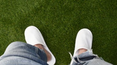 Spor ayakkabılı genç bir kadın ve yeşil çimlerde kot pantolon.