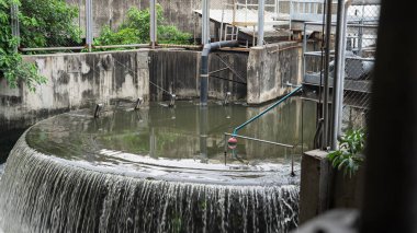 Çalışan bir atık su arıtma tesisini çevreleyen yarı bel yüksekliğindeki beton çit atık su arıtma istasyonunun resmi. Su seviyesi yükseltildi. Havuzun kenarından akan 