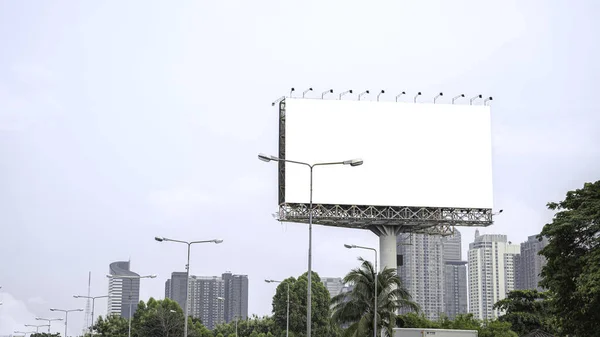 Image of a large advertising billboard on the side of the road. It is taller than an electric pole. and was as wide as a 2-lane road, raised to a towering height Among the skyscrapers in the big city