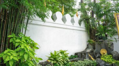 Üzerinde sarı bir bayrak asılı duran antik beyaz şehir duvarının görüntüsü. Önünde bambu kemeri ve süslü ağaçlar var. Küçük, gölgeli bir bahçe gibi diktim..