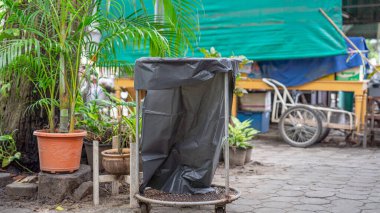 Ekonomik çöp tenekesi çelik çerçeve için siyah bir çanta kullanıyor. Kullanımı kolay, taşınması kolay ağaç kutusunun yanındaki bir dükkanda. Küçük bir bahçe köşesine yerleştirilmiş, illüstrasyon için uygun. 