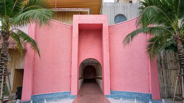 The artificial building is painted a distinctive pink color. Its shape is concave. The door has a high square edge. And the curved shape at the bottom makes the picture look dimensional.