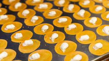 Açık kahverengi küresel hamur işi tabaklar büyük, yarı boyutlu metal dikdörtgen bir sobanın üzerine yerleştirilmiş. Merkezin beyaz kremsi bir dokusu var. Tatlı bir tadı var ve popüler bir tatlı.