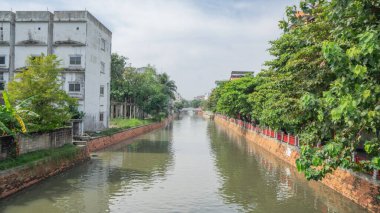 Nehirlerin ve kanalların göz alabildiğince uzadığı yerlerde beyaz bir feribot köprüsü var. Kıyı boyunca birçok büyük yeşil ağaçlar var. Yüksek katlı bir binanın yanında.