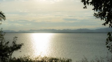 Peyzaj fotoğrafçılığı gölün berrak suları akşam güneşini yansıtır. Gökyüzü donuk bir renkti ve bir sürü bulut vardı. Uzaktan dağları görebilirdiniz.