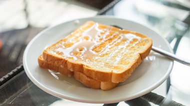 Popüler kahvaltı fotoğrafları. Kenarlı dilimlenmiş ekmek. Tost güzel kızartılmış. Üzerinde beyaz tatlandırılmış konsantre süt var. Tatlı ve lezzetli görünüyor. Temiz beyaz tabakta servis edilmiş. Parlak bir gümüşle