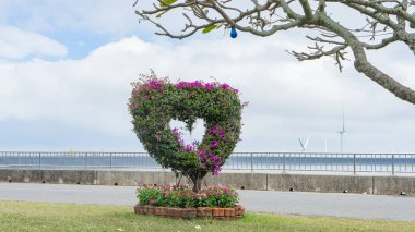 Yapay ağaç, kablodan yapılmış bir yapı kullanarak yere kalp şeklinde çiçekler dikiyor ve üssün etrafındaki alanda ek süslemeler var. Parkın kıyısında, rezervuarın yanında.