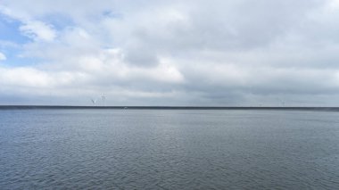 Büyük su depolama tankı göz alabildiğince ufka paralel temiz gökyüzüne bakar. Yumuşak beyaz yoğun kümelenmiş bulutlar vardır. Su yüzeyi düzensiz. Işıktan ve ışıktan etkilenmiş
