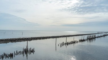 Taş ve kütüklerden oluşan bir duvar resmi. Denizi engellemek için yapılmış. Gün boyunca düzenli ve güzel olan tatlı suyla buluşmak için akan gökyüzünde bulutlar ve güneş ışığı parlıyordu.