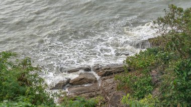 Deniz kenarındaki kayalıklarda hem küçük hem de büyük bloklar var. Suyla yıkanan bir uçurum var. Su bariyeri görevi gören bir uçurum. Ve eğilen deniz kenarındaki ağaçlar.