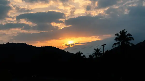 evening sky photography Sunset, bright light, blue sky with clouds blocking the sun. Orange light pierces the clouds Among the natural scenery, mountains, dark forests Mysterious, quiet atmosphere