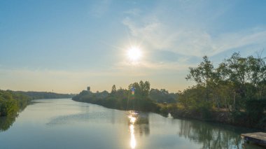 Ufkun üzerinde yükselen sabah güneşinin görüntüsü berrak bir göletin kenarında suyun içinde güneşin yansıması var. Dünyaya ışık saçan çeşitli kitlelerin arasından.