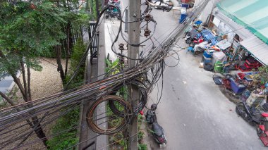 Elektrik direklerine dolanmış yüksek voltajlı kabloların görüntüsü aşağıdaki dar bir geçitten geçen küçük bir yol. Yakınlarda bir bakkal var..