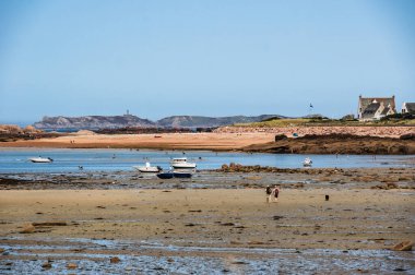 Güneşli bir yaz gününde, Brittany 'nin Tregastel plajının manzaralı sahili, masmavi suları ve kayalık kıyıları var..