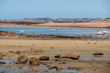 Güneşli bir yaz gününde, Brittany 'nin Tregastel plajının manzaralı sahili, masmavi suları ve kayalık kıyıları var..