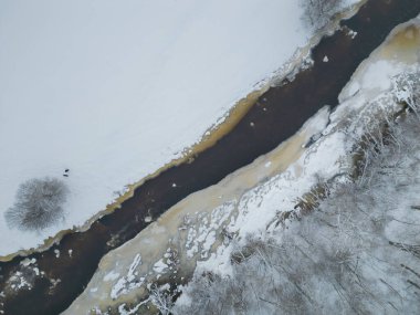 İnsansız hava aracı görüntüsü, kış sahnesi, Estonya doğası. Nehir karla kaplı bir tarla ve ormanın içinden akar. Yüksek kalite fotoğraf