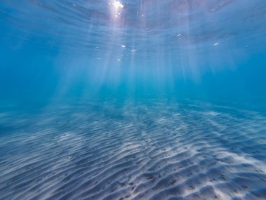 Sandy bottom on the beach in Greece, the sun's rays break through the water. Underwater photo. High quality photo