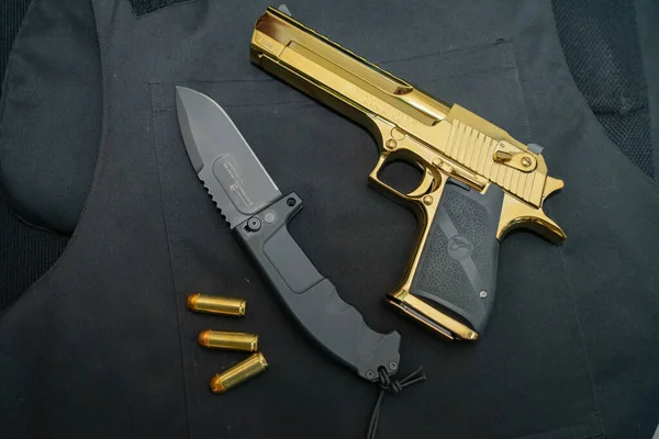 Estonia, Tallinn August 15, 2023. A powerful Desert eagle 50AE gold-colored pistol and an Italian long-range reconnaissance knife Extrema ratio rao 2. High quality photo