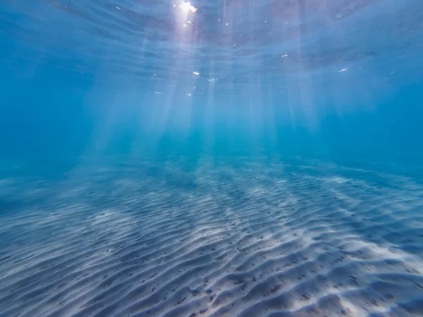 Sandy bottom on the beach in Greece, the sun's rays break through the water. Underwater photo. High quality photo