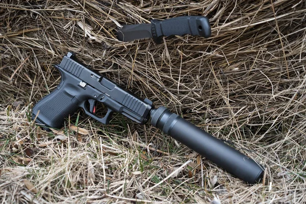 A pistol with a silencer and a knife with a fixed blade near a sheaf of hay. High quality photo