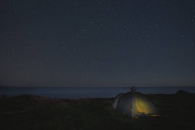 Gece sahnesi, Paldiski 'de dik bir deniz kıyısında yıldızlı gökyüzünün altında çadırla kamp yapmak. Yüksek kalite fotoğraf