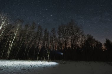 Kış gecesi ormanında fenerli bir erkek yolcu. Peyzaj astrofotoğrafçılığı. 
