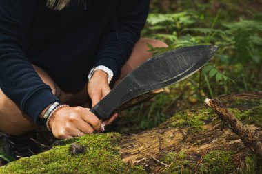 A girl holds a kukri sword in her hands outdoors in the forest for chopping wood.  clipart