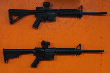 Two unloaded M4A1 rifles on an orange wall in a shooting range.  clipart