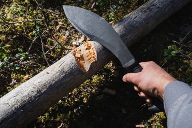 A large black tactical kukri knife for chopping wood in a man's hand in the forest. clipart