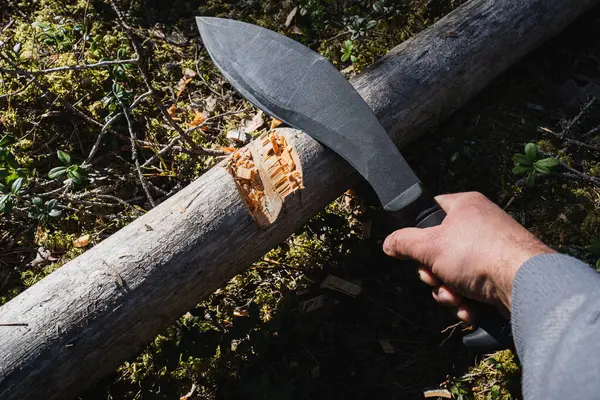 stock image A large black tactical kukri knife for chopping wood in a man's hand in the forest.