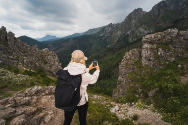 Sırtında sırt çantası olan bir gezgin kız telefonuyla fotoğraf çekiyor. Bir yaz akşamı Polonya Tatra Dağları 'nda, gökyüzü bulutlu.. 