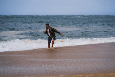 Güneş gözlüklü ve elbiseli Avrupalı bir adam okyanustaki dalgalardan kaçar.. 