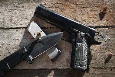 Classic M1911 pistol and folding knife on an old wooden surface in an abandoned building. clipart